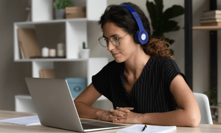 Woman wears headphones while looking attentively at a laptop screen.